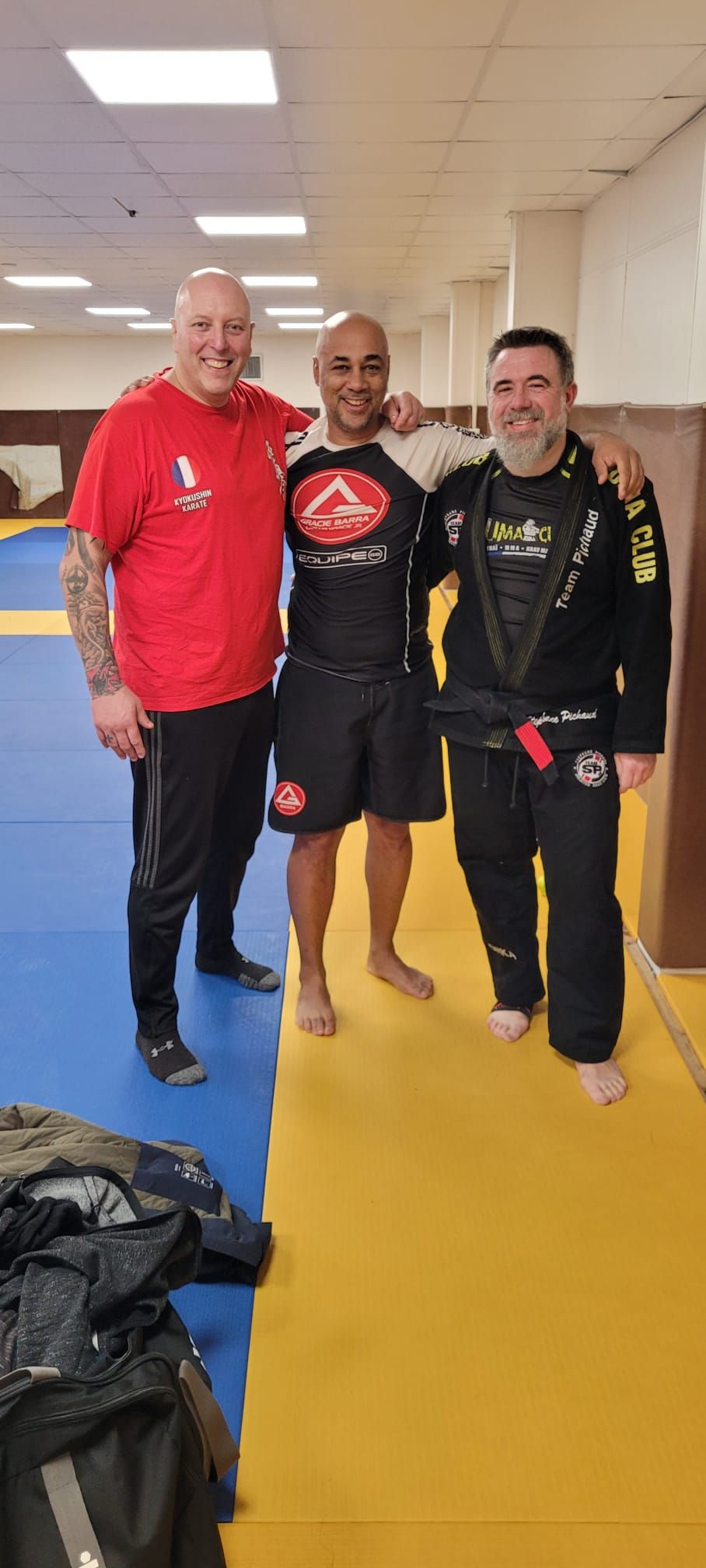 Trois pratiquants souriants sur le tatami, dont l'un en kimono noir du Puma Club.